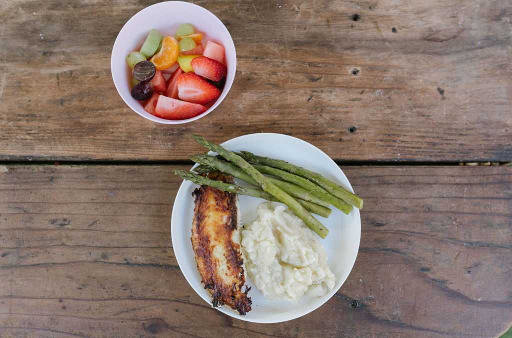 Asparagus with mashed potatoes and fish and fresh fruit in a bowl.