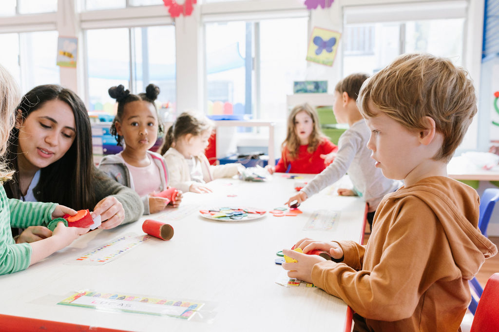 ABS Pre-School teacher with kids at a table doing crafts.