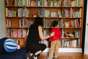 A teacher helping a student find a fun book to read on a big shelf of kids books
