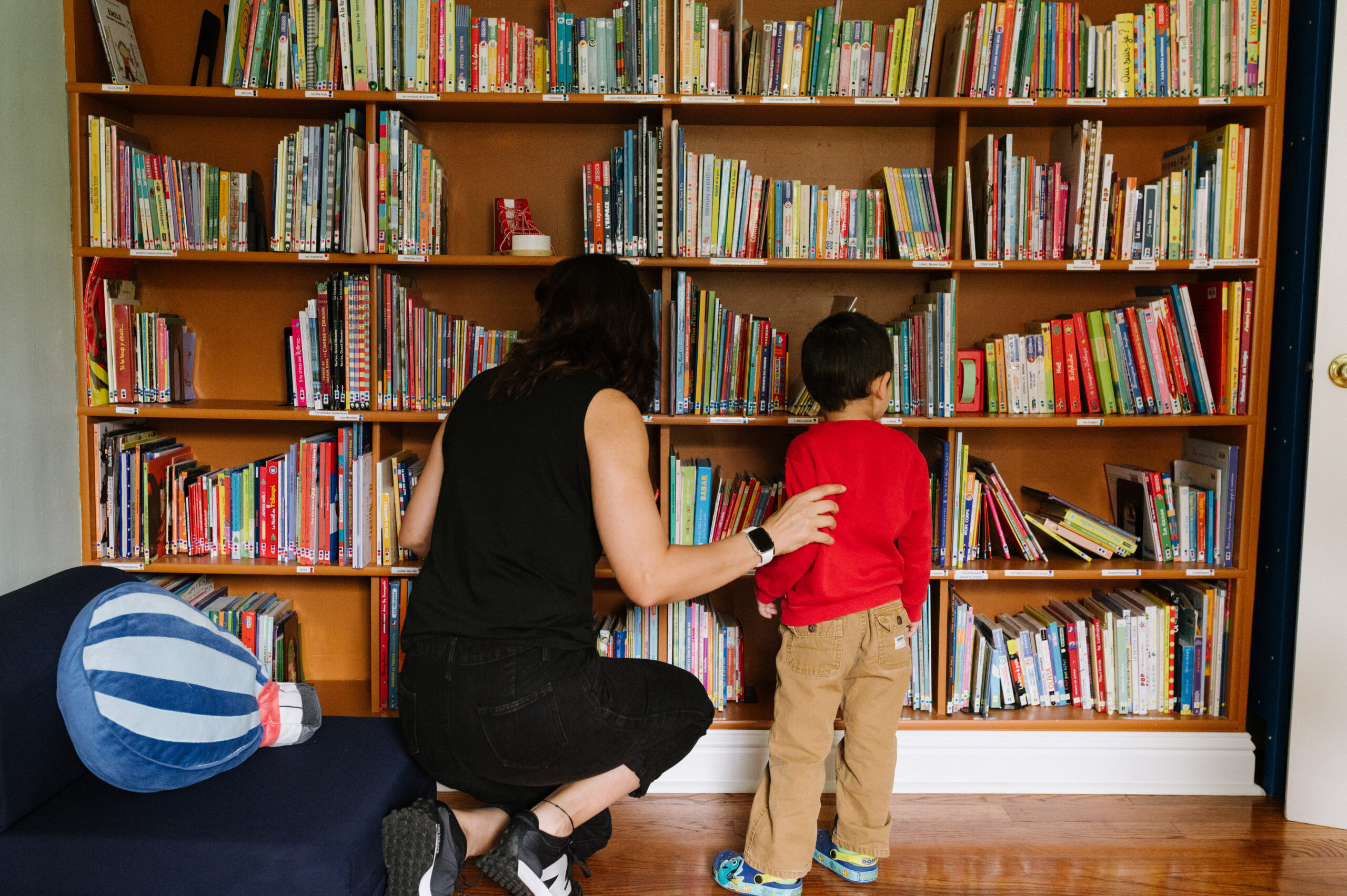 A teacher helping a student find a fun book to read on a big shelf of kids books
