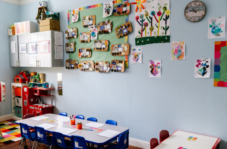 A classroom with neat tables ready for students and an art wall full of children's fingerpaints