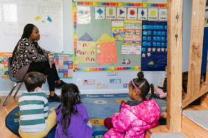 Kids listening to their teacher who is sitting in a chair