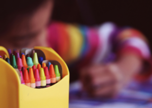 An up-close shot of crayons with a student coloring in the background