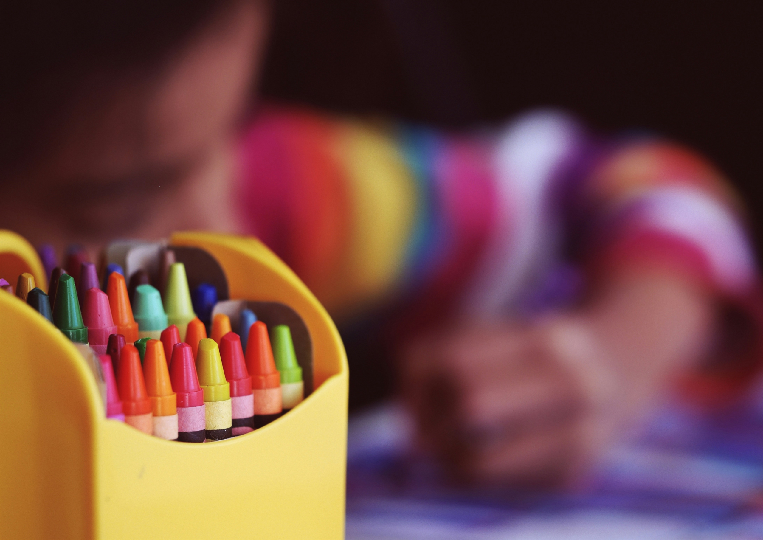 An up-close shot of crayons with a student coloring in the background