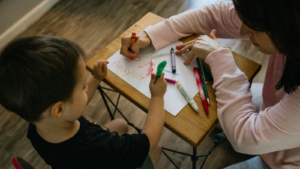A teacher sitting with a student as they draw on a paper