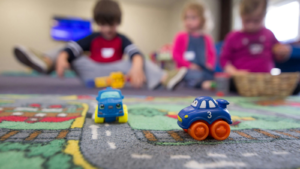 Close-up of two toy trucks with preschool kids in the background