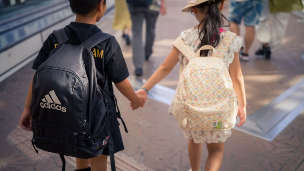 Two kids holding hands walking to school with backpacks on