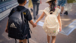Two kids holding hands walking to school with backpacks on