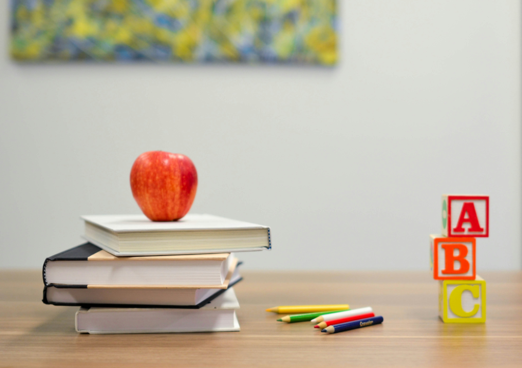 A classroom desk with books, an apple, and letter blocks