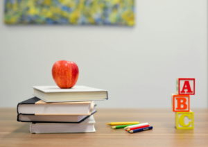A classroom desk with books, an apple, and letter blocks